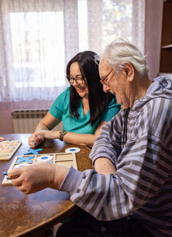 Nurse Helping Out Senior Male with Dementia Play with Tic-Tac-Toe Healthcare worker encouraging a senior with dementia to participate in a game of tic-tac-toe, promoting mental stimulation and connection