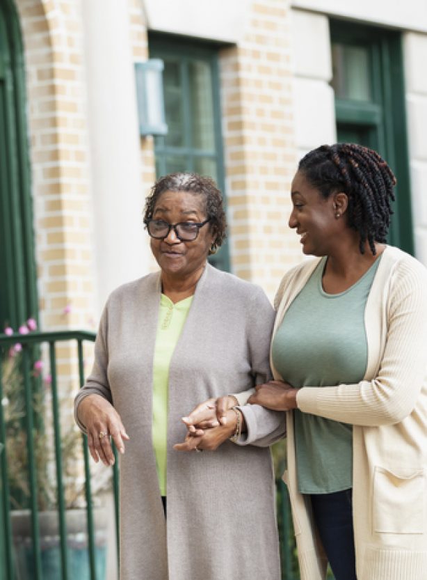 A senior African-American woman walking arm in arm, holding hands with her adult daughter down a sidewalk in a residential neighborhood in the city. Mother is in her 70s and her daughter is a mature woman in her 40s.