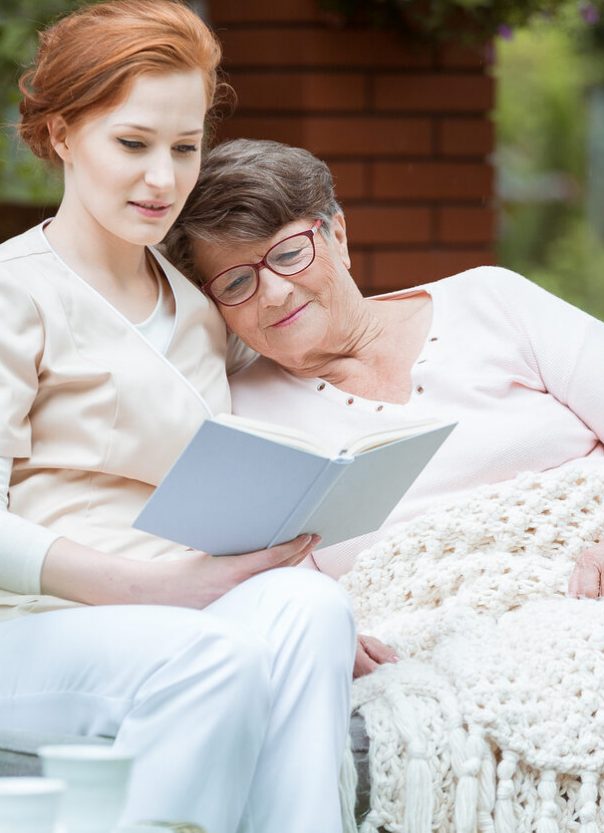Elder lady in glasses covered with blanket resting her head on nurse's shoulder