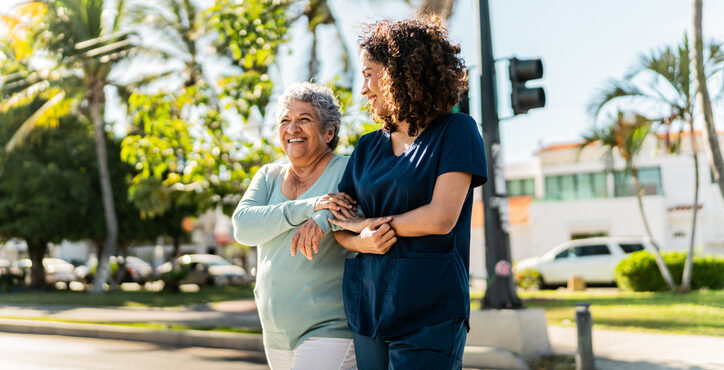Home caregiver and senior woman walking and talking outdoors