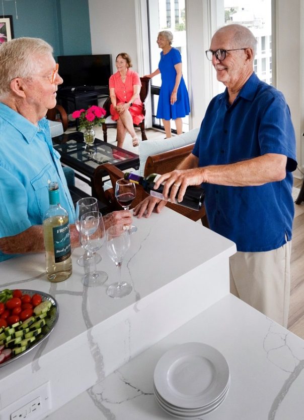 male couple stands pouring wine in kitchen during cocktail party