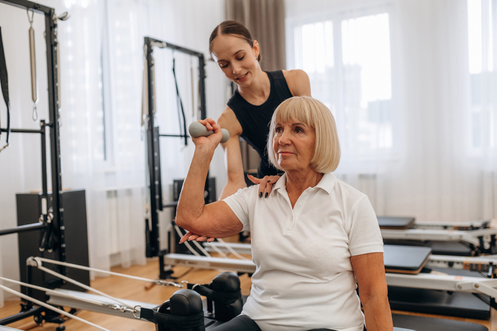 Female trainer is helping senior woman with arm exercises.