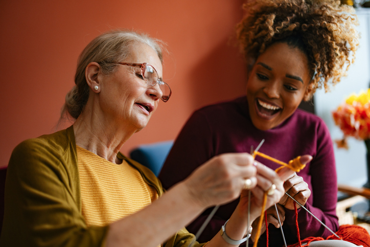 Joyful Senior Woman Knitting With Young Caregiver