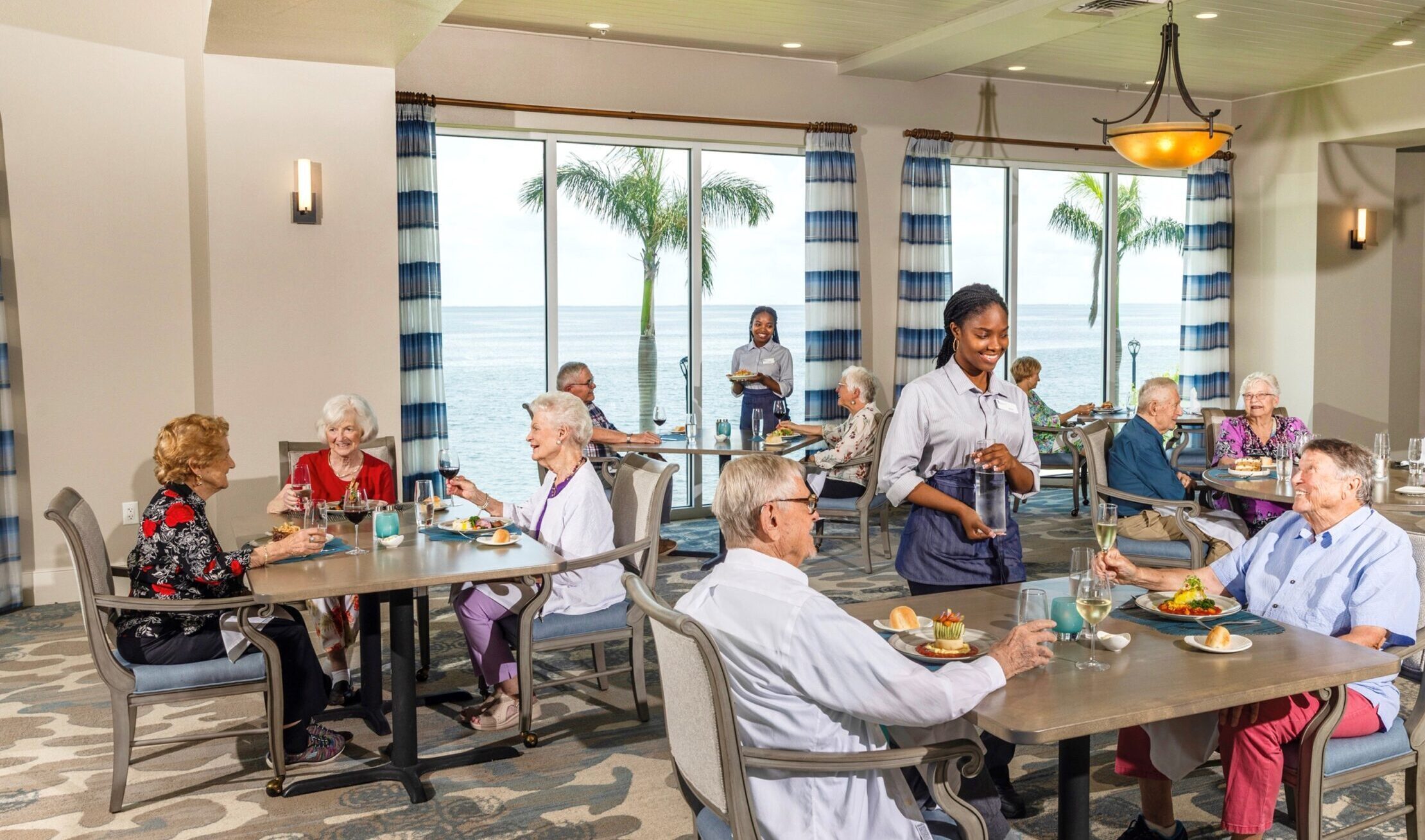 men and women and women site in upscale dining room with floor to ceiling windows overlooking Little Bayou in St. Petersburg