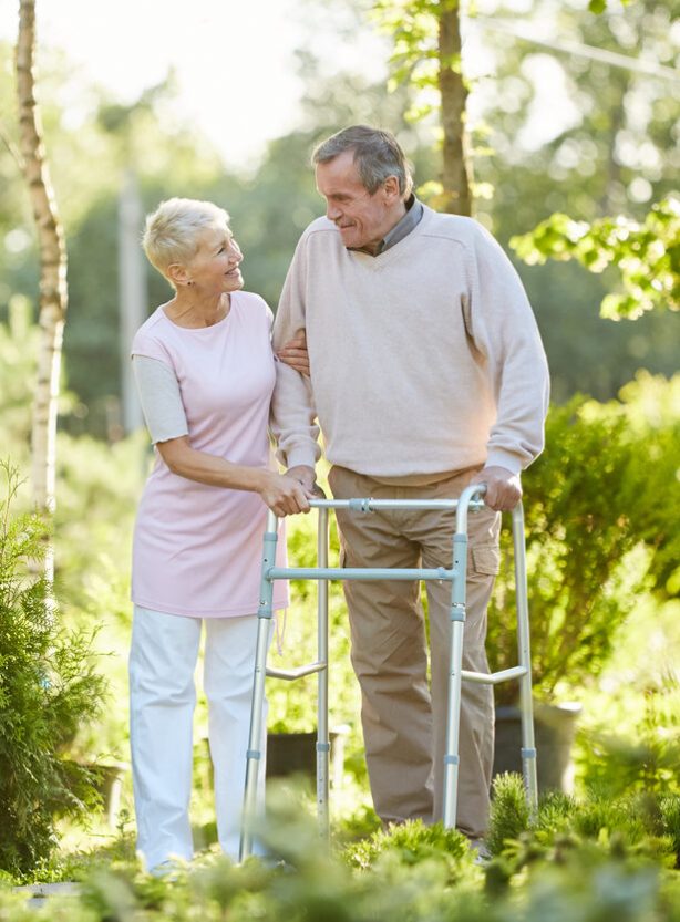 Full length portrait of senior man walking in hospital park with wife, copy space