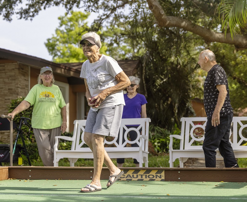 woman in visor smiles on bocce court while scoping shot with friends in background