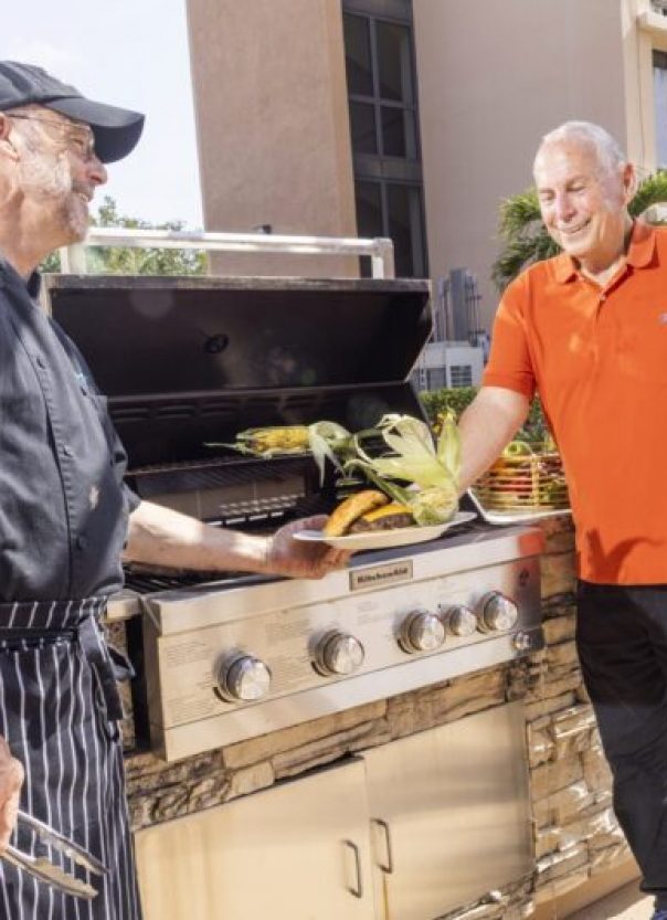 SUN – Dining – Savour-min Senior man taking plate with grilled corn and burger from chef at cookout