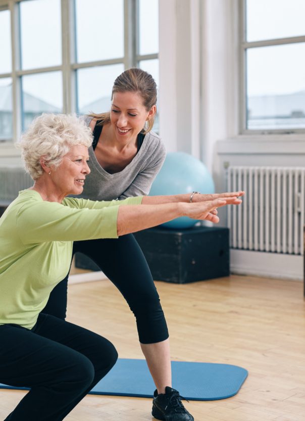 Elderly woman doing exercise with her personal trainer at gym. Gym instructor assisting senior woman in her workout.