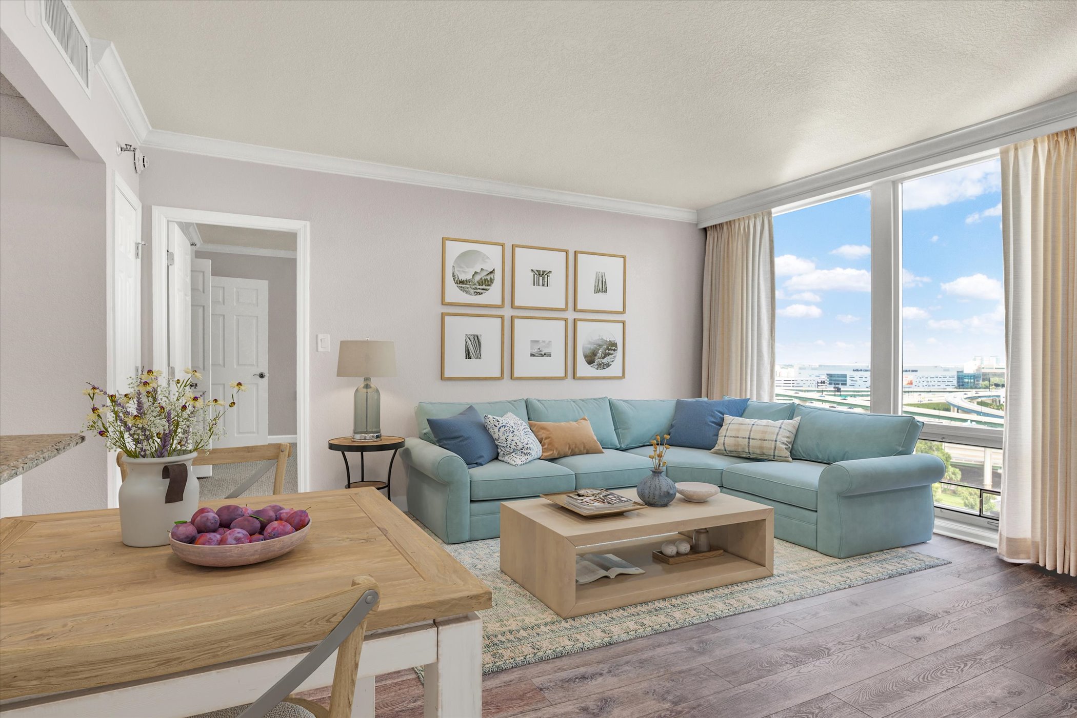 Bright, large living room with sectional featuring floor to ceiling windows and open kitchen