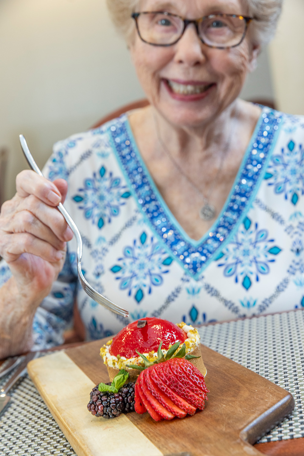 Senior woman smiling holding a fork over a strawberry torte dessert