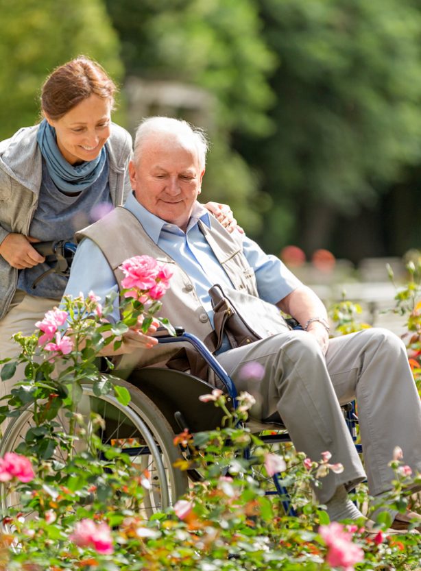 Caregiver and senior man on a wheelchair walking outdoors in a park