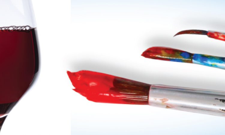 A glass of red wine to the left of three wet paintbrushes