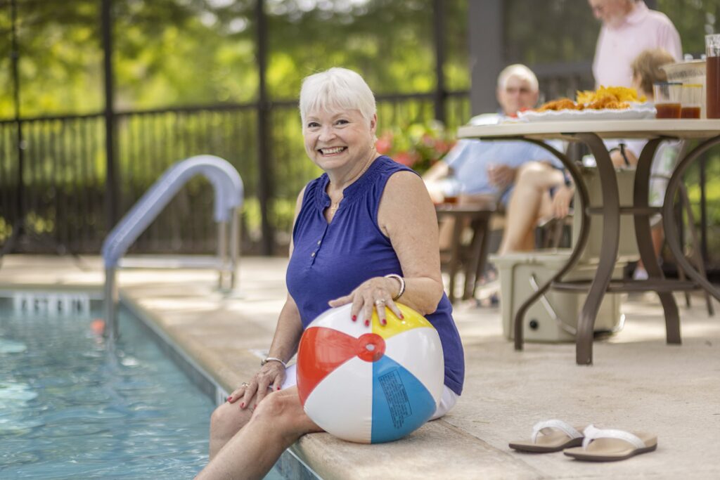 Senior sitting with beach ball while dipping feet into pool