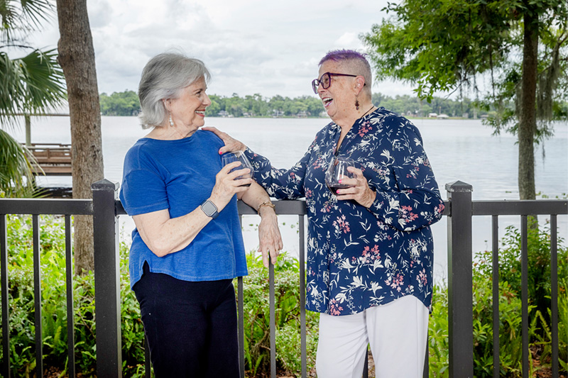 Two senior women smiling drinking wine in front of a river view