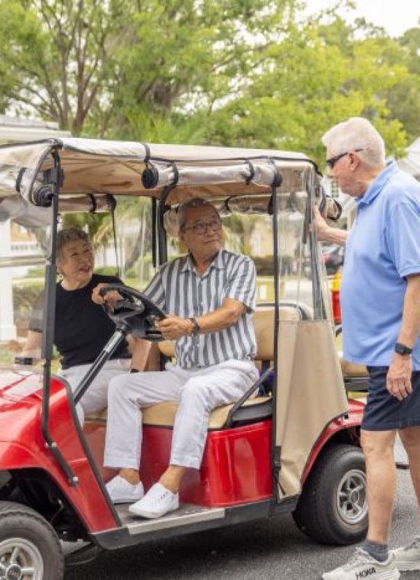Seniors riding in golf cart greeted by friends