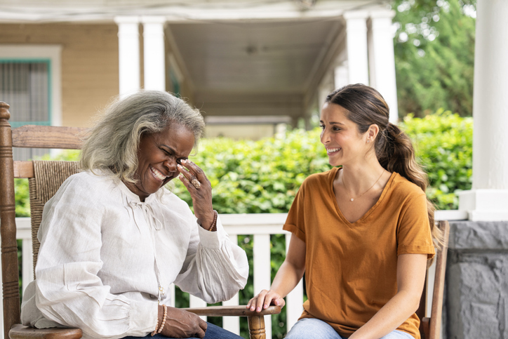 Cheerful senior woman chatting with young female caregiver in comfortable assisted living facility.