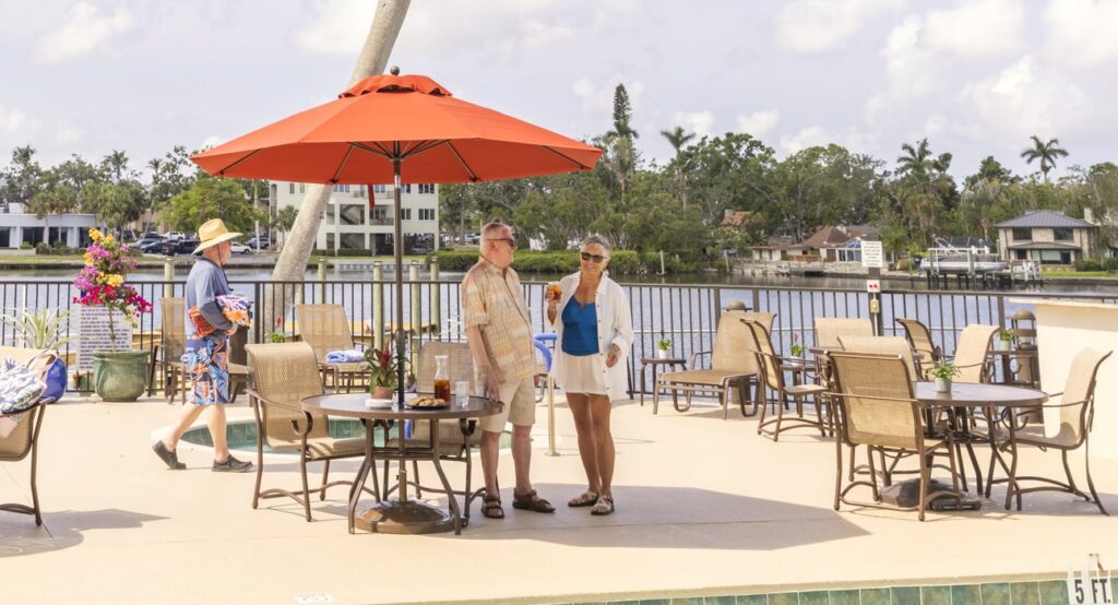 couple stands under umbrella drinking tea at pool party