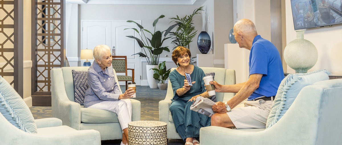 two women sit in lobby with coffee showing a photo on a cell phone to a seated man