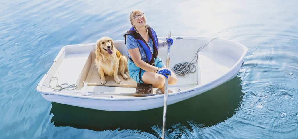 woman in row boat with golden retriever smiles up at the sky