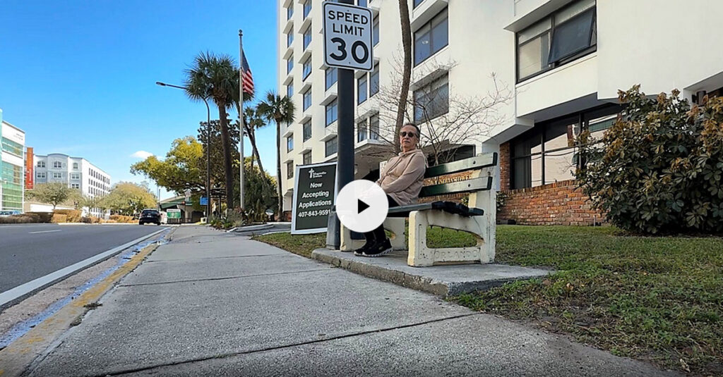 Senior woman sitting on sidewalk bench waiting for a shuttle bus