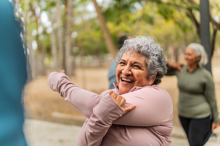 Senior woman stretching and talking friend at public park