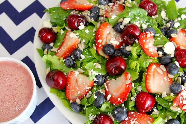 colorful green salad covered with blueberries, strawberries, and cherries