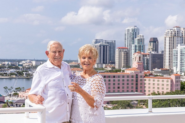 smiling man and woman stand on rooftop patio overlooking downtown St. Petersburg and Tampa Bay