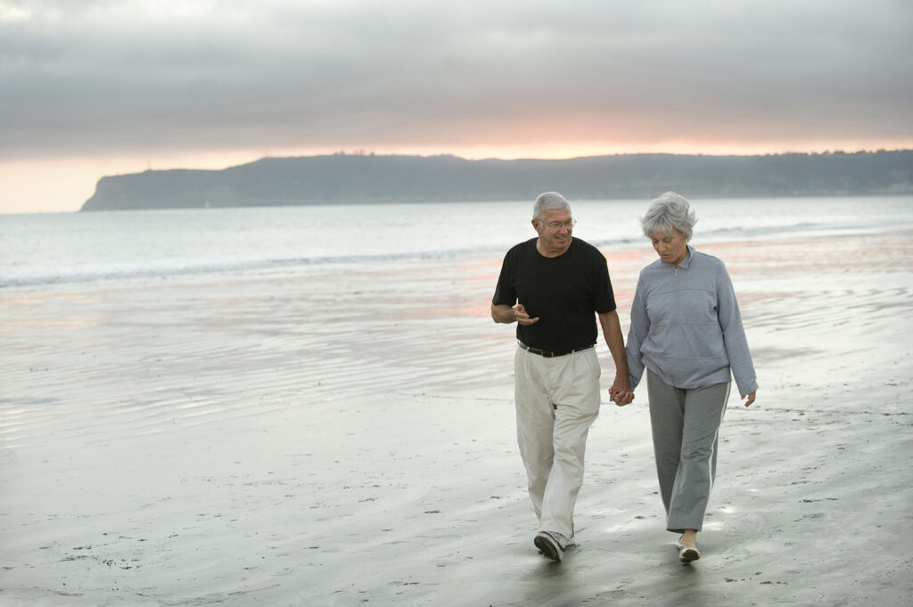 Senior couple walks along the beach at sunrise.