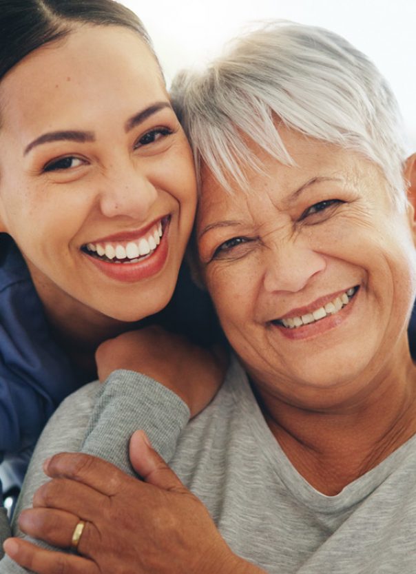 A caregiver and a senior woman embrace with big smiles