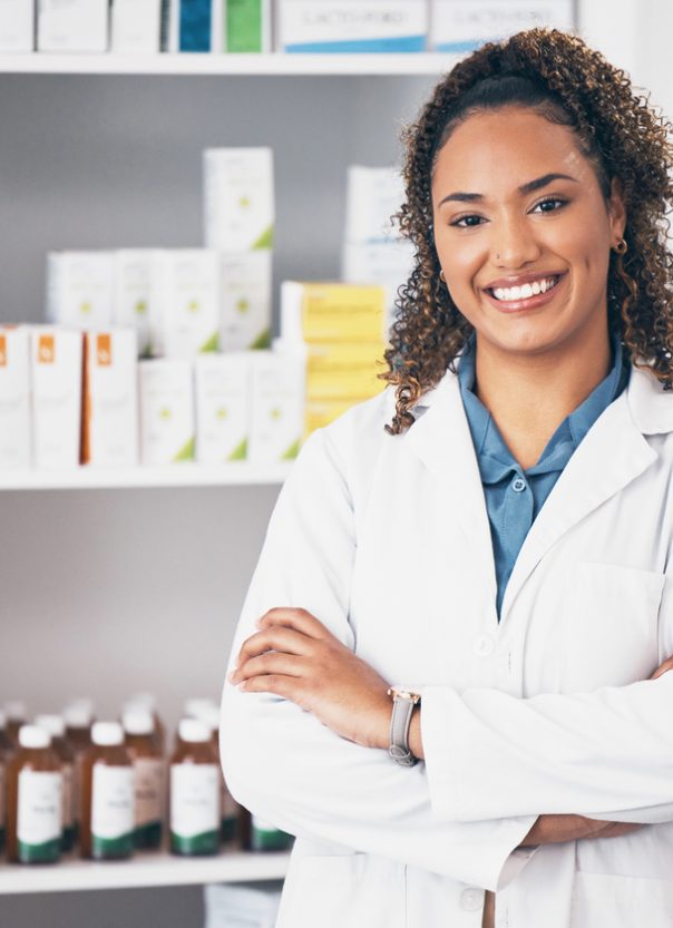 Pharmacy, pharmacist or portrait of woman with arms crossed or smile in customer services or clinic. Healthcare help desk, wellness or happy doctor smiling by medication on shelf in drugstore Pharmacist
