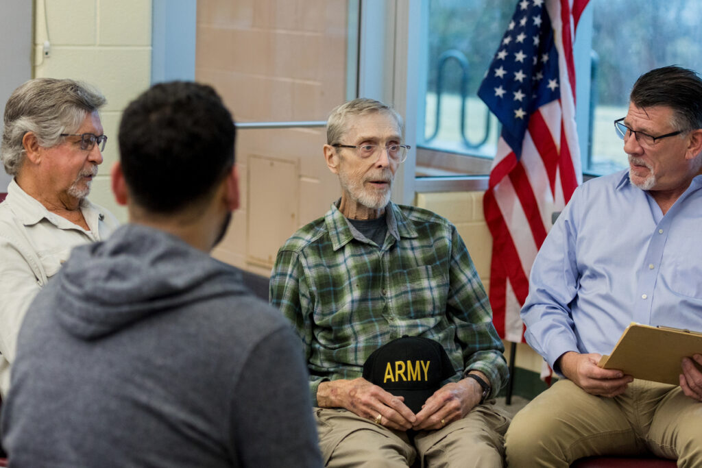 Group therapy session; men discussing experiences, showing empathy and support.